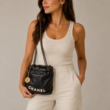 Model wearing the Chanel 22 bag in black calfskin crossbody with gold-tone chain and medallion